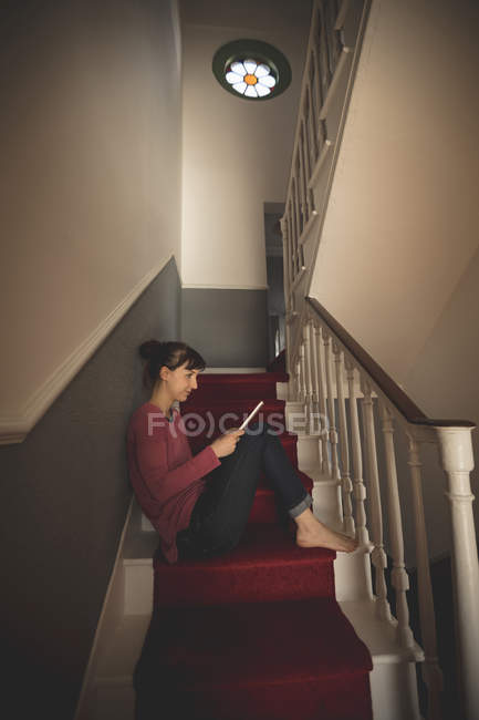 Woman using digital tablet on staircase at home — Stock Photo