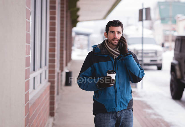 Junger Mann telefoniert mit Handy, während er auf der Straße Kaffee trinkt. — Stockfoto