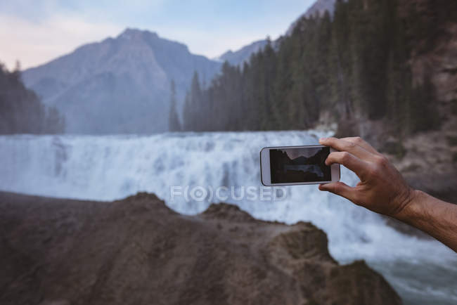 Primer plano del hombre tomando fotos de la cascada con el teléfono móvil - foto de stock