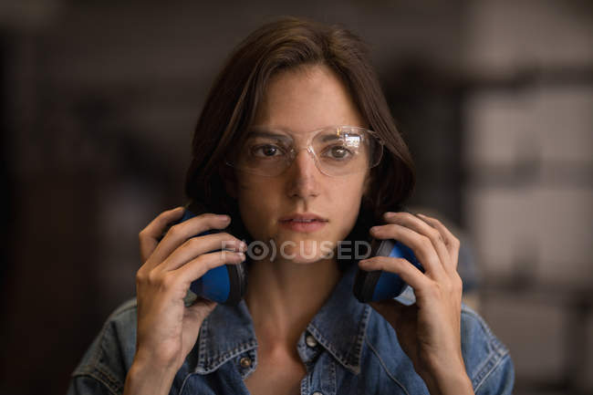 Thoughtful female artisan with earmuffs in workshop. — Stock Photo