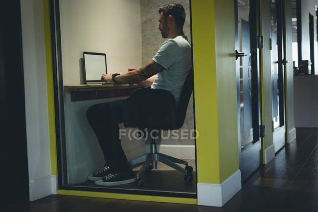 Бизнесмен, использующий ноутбук в кабине в офисе — стоковое фото