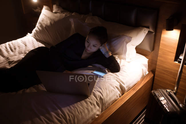 Femme utilisant un ordinateur portable sur le lit à l'hôtel — Photo de stock