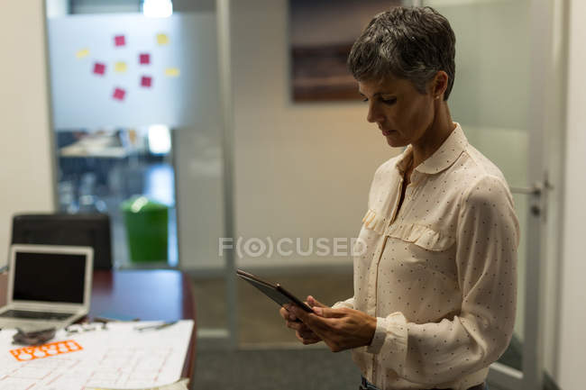 Зрелая деловая женщина, использующая цифровой планшет в офисе — стоковое фото