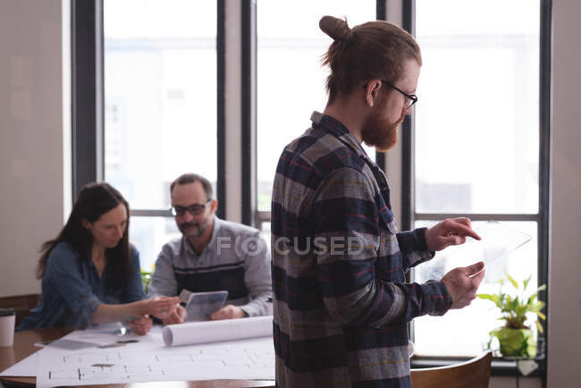 Мужчина руководитель с использованием стеклянной цифровой планшет в интерьере офиса с коллегами, работающими в фоновом режиме — стоковое фото