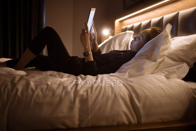 Donna che utilizza tablet digitale mentre si rilassa sul letto in hotel — Foto stock