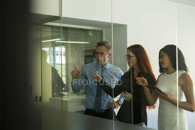 Compañeros de negocios discutiendo sobre tablero de vidrio en la oficina - foto de stock