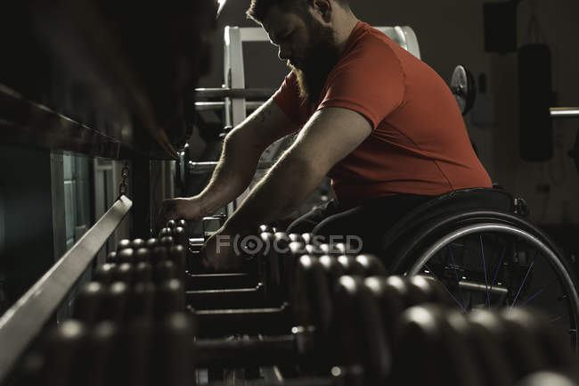 Deficiente homem em cadeira de rodas levantando halteres de rack no ginásio — Fotografia de Stock