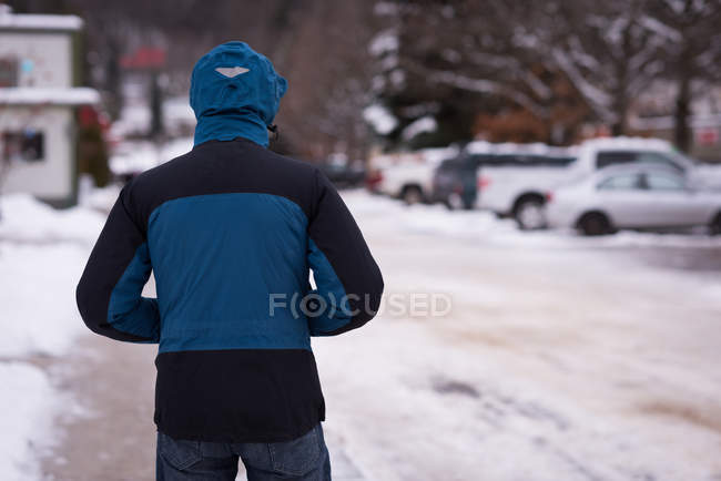 Вид ззаду чоловіка, що стоїть з руками в кишені на засніженій вулиці . — стокове фото