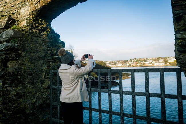 Mujer tomando fotos con teléfono móvil cerca de la orilla del río . - foto de stock