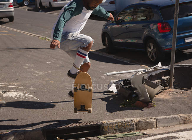 Uomo che salta sullo skateboard in strada alla luce del sole — Foto stock
