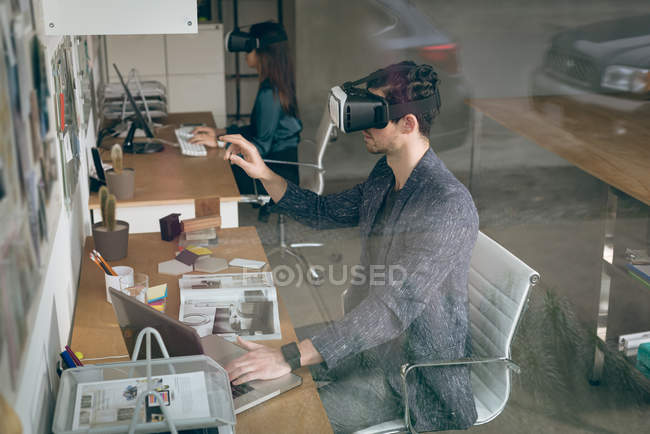 Exécutif travaillant sur un ordinateur portable tout en utilisant un casque de réalité virtuelle au bureau — Photo de stock