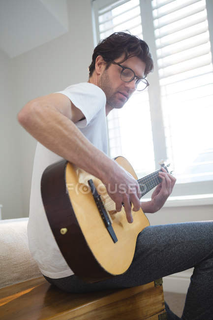 Hombre tocando la guitarra en el dormitorio en casa - foto de stock