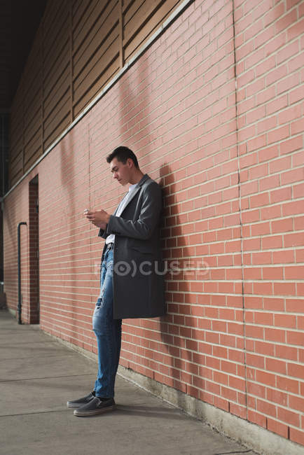 Uomo che utilizza il telefono cellulare mentre si appoggia al muro nel corridoio — Foto stock