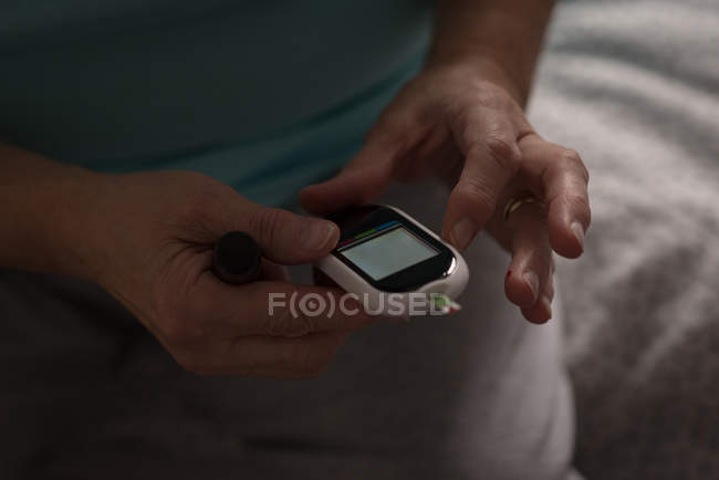 Senior woman checking blood pressure on a monitor at home — Stock Photo