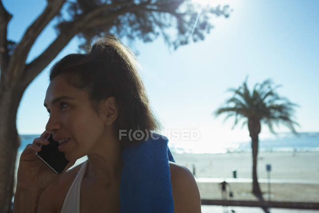 Жінка з рушником розмовляє на мобільному телефоні на тропічному узбережжі — стокове фото