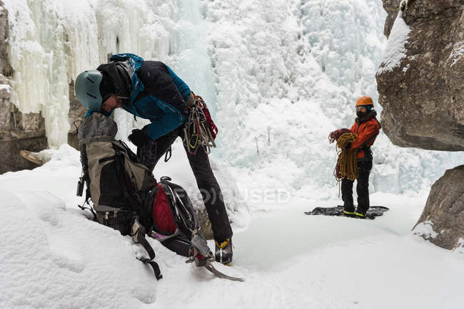 Male rock climber checking backpack near rocky ice mountain — Stock Photo