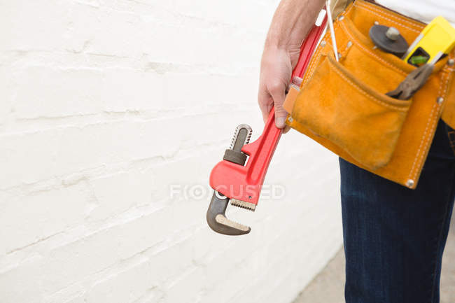 Mid section of male carpenter with tool belt holding clamp — Stock Photo