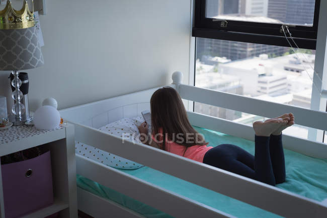 Дівчина використовує мобільний телефон у спальні вдома, вид ззаду — стокове фото
