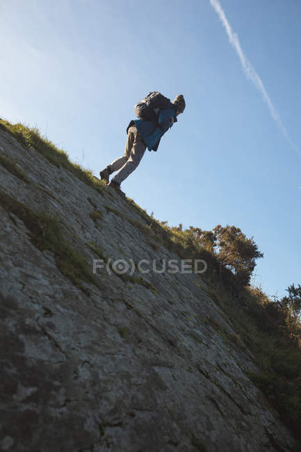 Escursionista di sesso maschile a piedi con zaino in collina in campagna alla luce del sole — Foto stock