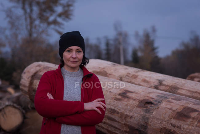 Portrait of woman standing with arms crossed against wood — Stock Photo