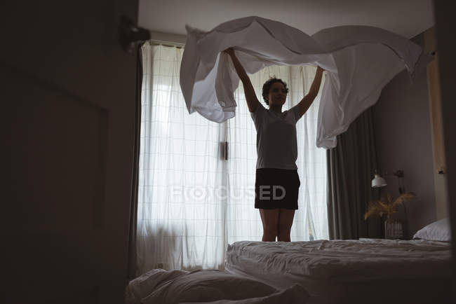 Молодая женщина разбрасывает постельное белье по кровати в спальне дома — стоковое фото