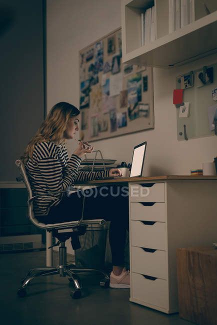 Female executive talking on mobile phone while working on laptop at desk in office — Stock Photo