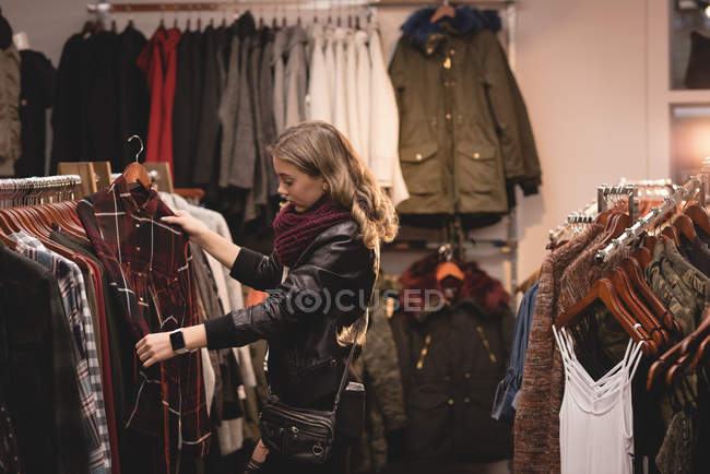 Hermosa chica seleccionando ropa de rack en el centro comercial - foto de stock