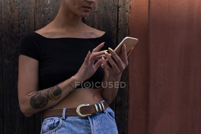 Mid section of young adult woman using mobile phone in front of wooden wall. — Stock Photo
