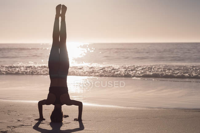 Fit mulher realizando headstand na praia ao entardecer . — Fotografia de Stock