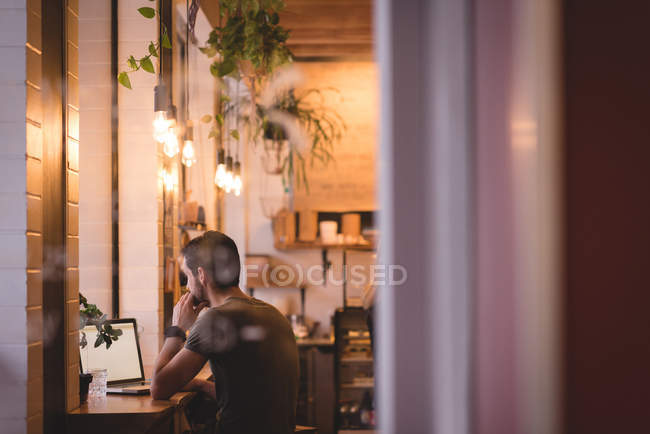 Side view of man using laptop in cafe interior. — Stock Photo