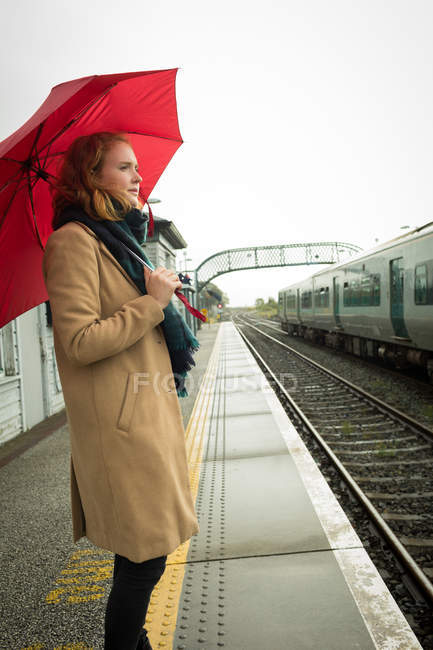 Giovane donna in piedi con ombrello alla stazione ferroviaria — Foto stock