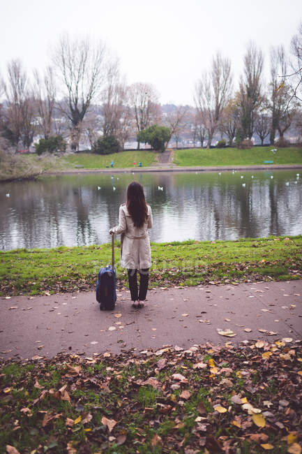 Вид спереду бізнес-леді з багажем, що стоїть біля берега озера — стокове фото