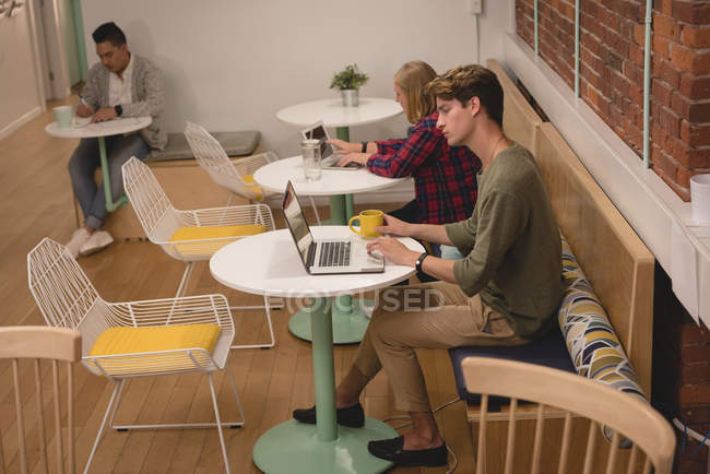 Homme exécutif utilisant un ordinateur portable à la cafétéria dans le bureau — Photo de stock