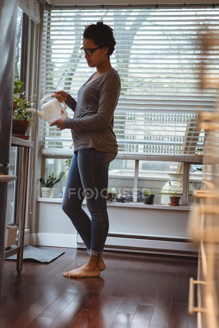 Mujer embarazada joven regando las plantas en casa - foto de stock