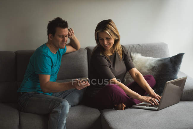 Пара використовує ноутбук і мобільний телефон у вітальні вдома — стокове фото