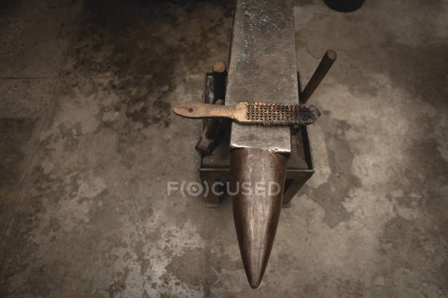 Cepillo de alambre de mano mantenido en yunque en taller - foto de stock