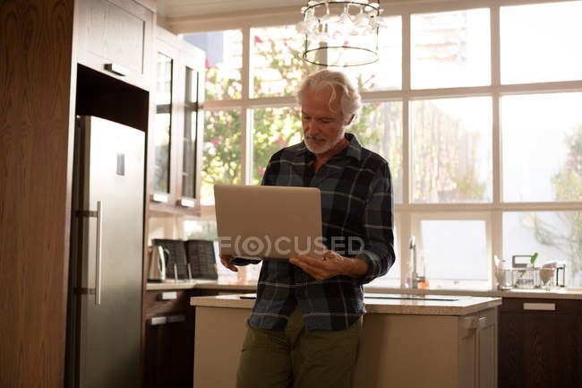 Homme âgé utilisant un ordinateur portable dans la cuisine à la maison — Photo de stock