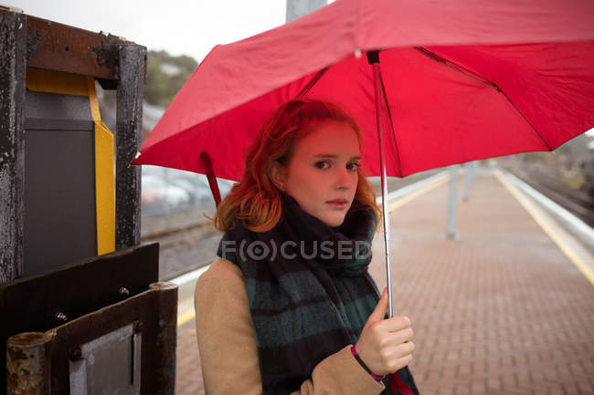 Jovem mulher com guarda-chuva à espera de trem na plataforma — Fotografia de Stock