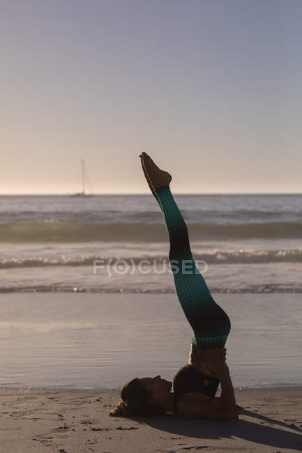 Подходящая женщина, занимающаяся йогой на пляже в сумерках . — стоковое фото