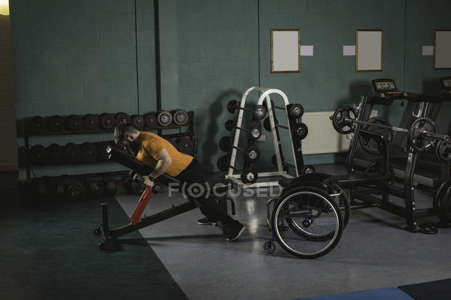 Інвалідний чоловік займається з гантелями на лавці прес в спортзалі — стокове фото