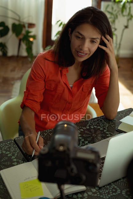 Женский видео блоггер пишет в дневнике перед камерой дома — стоковое фото