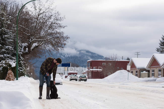 Homme caressant chien dans la rue enneigée pendant l'hiver . — Photo de stock