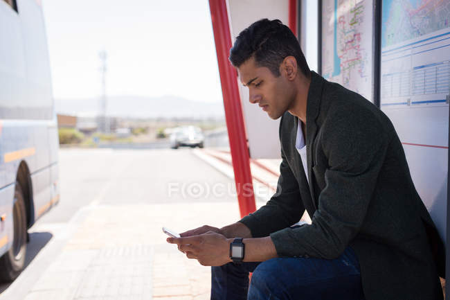 Jeune homme d'affaires utilisant un téléphone portable à l'arrêt de bus — Photo de stock