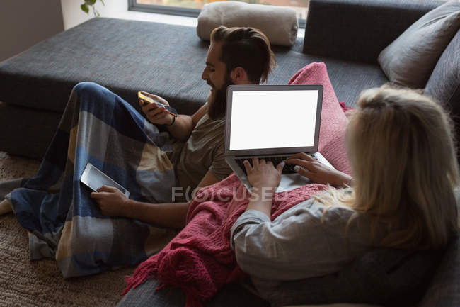 Женщина с ноутбуком, в то время как мужчина разговаривает по мобильному телефону в гостиной дома — стоковое фото
