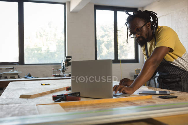 Carpenter using laptop at table in workshop — Stock Photo
