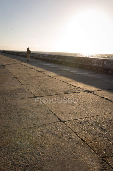 Vista posteriore della donna che cammina sul lungomare in luce soffusa — Foto stock