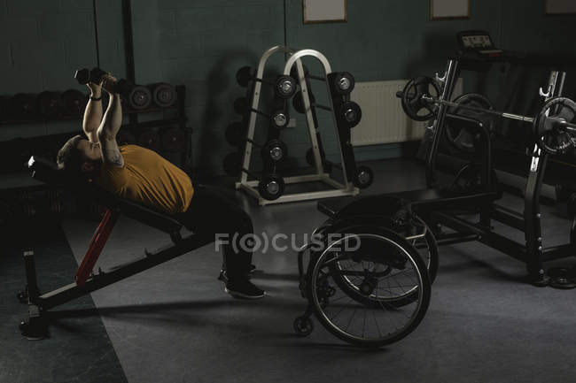 Handicapped man exercising with dumbbells on bench press in gym — Stock Photo
