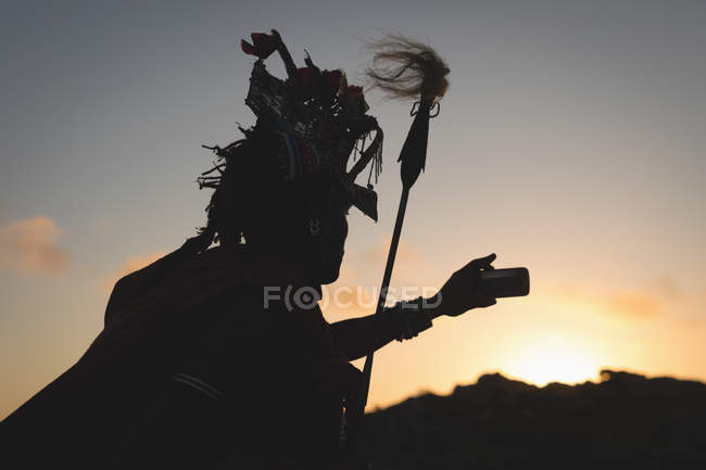 Silhouette eines Massai-Mannes, der in der Abenddämmerung ein Selfie mit seinem Handy macht — Stockfoto