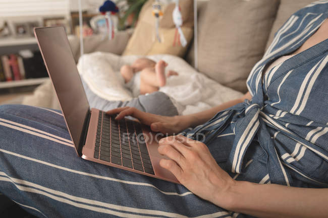Mutter arbeitet an Laptop-Baby, das neben ihr zu Hause im Kinderbett liegt — Stockfoto