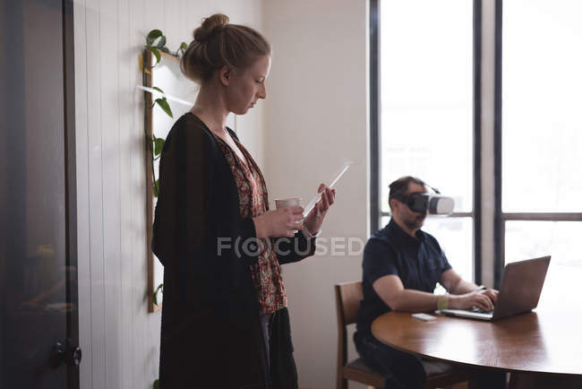 Collèges d'affaires utilisant une tablette numérique en verre, un casque de réalité virtuelle et un ordinateur portable au bureau — Photo de stock